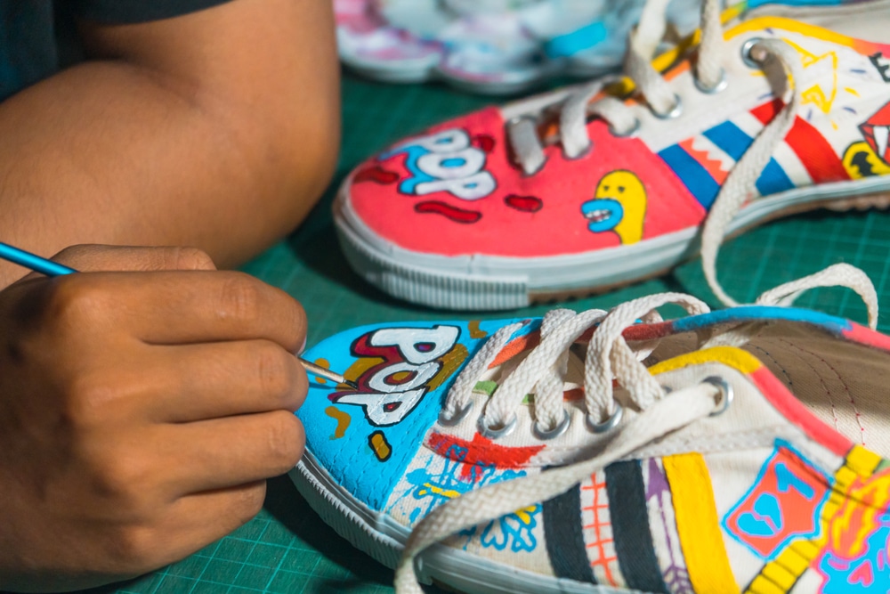 Sleman, Yogyakarta, Indonesia - December 21, 2020: The art of painting shoes made of white canvas using enamel paint with a small brush, all done manually by the artist