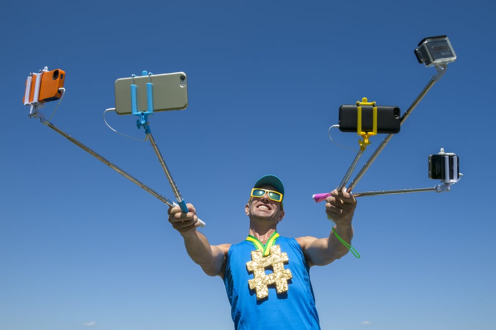 Hashtag gold medal athlete smiling for his many gadgets on selfie sticks as he poses for a picture