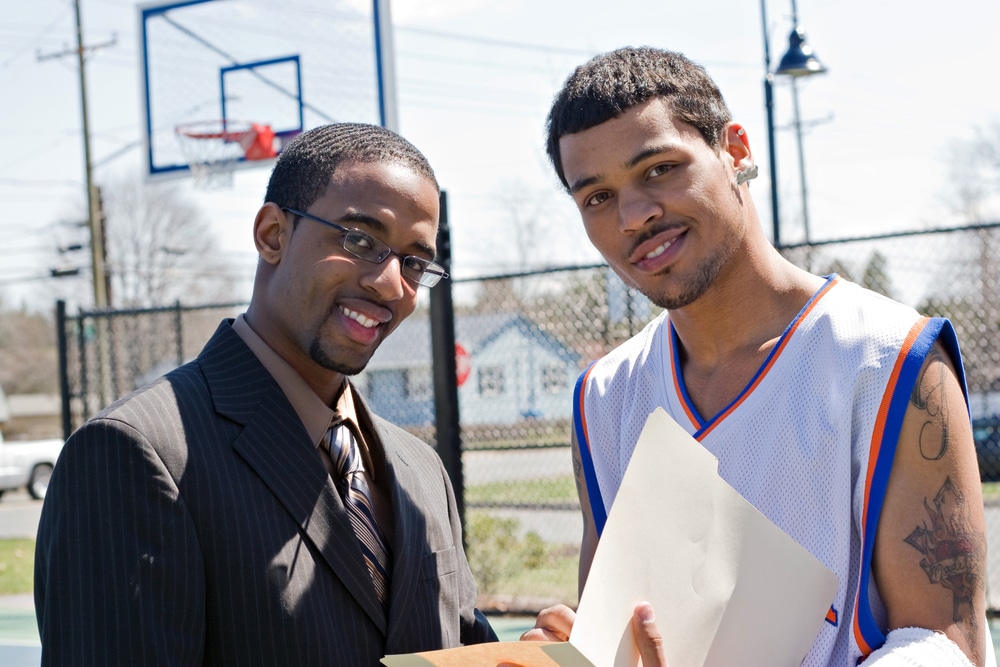 A basketball coach in a business suit sharing a play with a player on the team. He could be also be recruiter trying to get him to sign a contract.