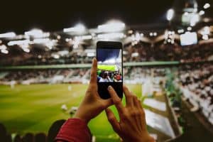 FanHandWithSmartphonePhotographingFootballMatchUsingMobilePhone - HQZ Fan hand with smartphone photographing football match. Using mobile phone camera at the stadium